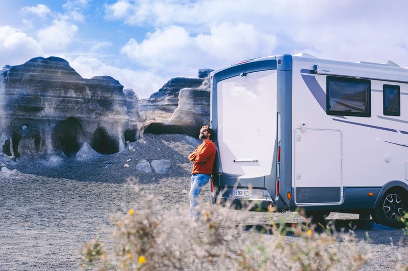 Person standing beside a travel trailer parked in a dramatic rock formation landscape